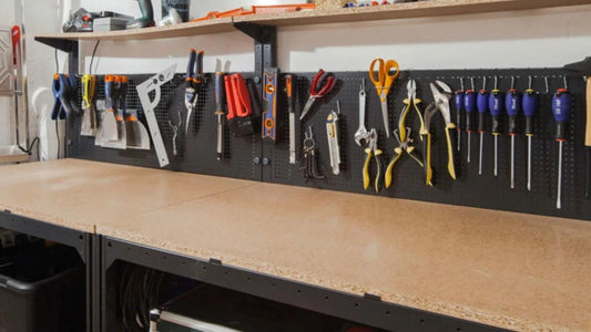 Différents outils de montage de meubles disposés sur un établi : perceuse-visseuse, tournevis avec embouts interchangeables, niveau à bulle, mètre ruban et clé à douille.